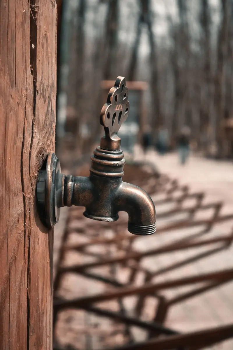 An antique brass water faucet mounted on a wooden post outdoors